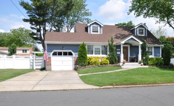 Blue single-family house with brown roof, white garage door, porch, American flag, and fenced yard.