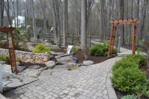 Stone pathway with wooden archways in a landscaped garden bordered by shrubs and trees.
