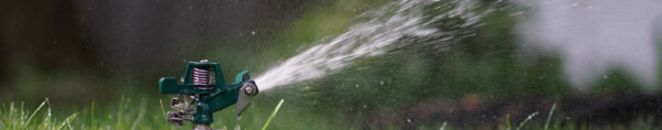 Green garden sprinkler spraying water over grass with a blurred natural background