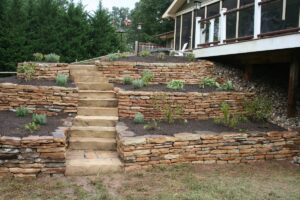 Terraced garden with stacked stone retaining walls, central stone steps, and small plants.