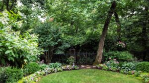 Neatly trimmed garden with curved flower bed, mixed flowers, shrubs, trees, and black metal fence.