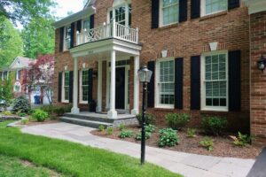 Brick house with black shutters, white porch columns, stone steps, and landscaped yard.