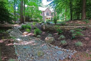 Brick house with landscaped garden, stone retaining wall, and dry rock bed surrounded by trees.