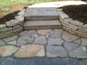 Stone pathway with irregular flagstones leading to two steps and low stone retaining walls.