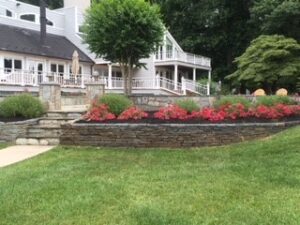 Residential property with multi-level house, stone retaining wall, red flowers, and green lawn.