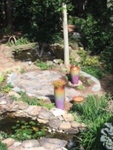 Landscaped garden with a small pond, lily pads, stone border, patio, and two tall ceramic pots.