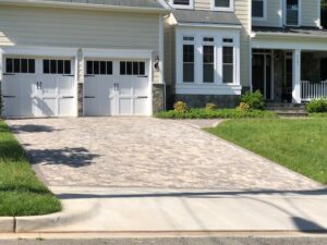 Residential house front with double garage, paved driveway, stone exterior, and green lawns.