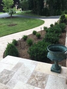 Curved paved walkway with stone steps, trimmed shrubs, mulched beds, and a decorative urn.