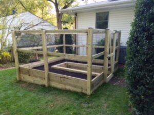 Raised wooden garden bed with railing and soil sections on grassy backyard near house.