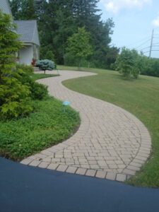 Curved brick walkway bordered by greenery and outdoor lights leading to a house.