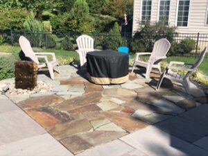 Backyard patio with four Adirondack chairs around a covered fire pit and a stone fountain.