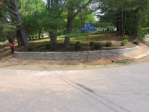 Street corner with stone retaining wall, grassy area, trees, street sign, and fire hydrant.