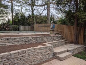 Terraced backyard with stone retaining walls, steps, wooden fence, and surrounding trees.