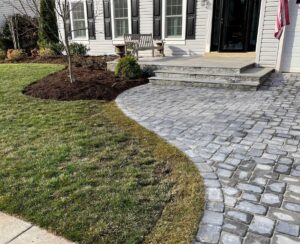 Stone-paved pathway curves from lawn to front porch with steps, bench, and American flag.