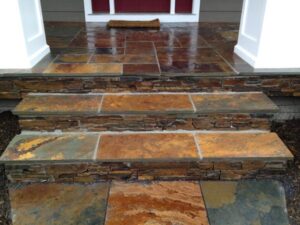 Stone steps and porch with stacked stone risers and a doormat in front of a door.