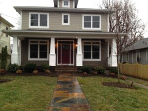 Two-story house with gray and beige siding, front porch, stone path, and landscaped lawn.