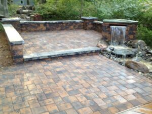 Outdoor patio with multi-colored stone tiles, raised stone wall, and waterfall water feature.