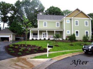 Two-story green house with white trim, covered porch, curved driveway, detached garage, and landscaped lawn.